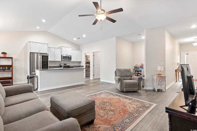 living room with light hardwood / wood-style floors, vaulted ceiling, and ceiling fan