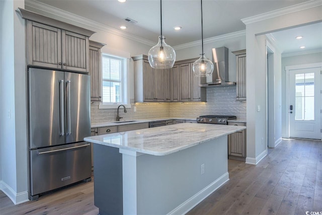 kitchen featuring wall chimney exhaust hood, high end fridge, sink, light stone counters, and a kitchen island