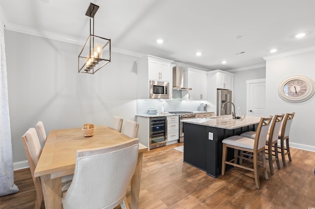 kitchen with wall chimney exhaust hood, a center island with sink, appliances with stainless steel finishes, beverage cooler, and white cabinets