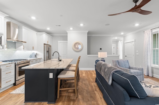 kitchen featuring premium appliances, wall chimney range hood, an island with sink, and white cabinets