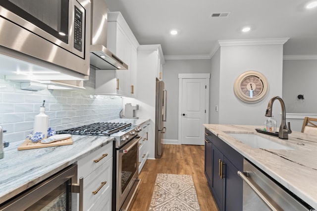 kitchen featuring appliances with stainless steel finishes, sink, wine cooler, white cabinets, and wall chimney exhaust hood