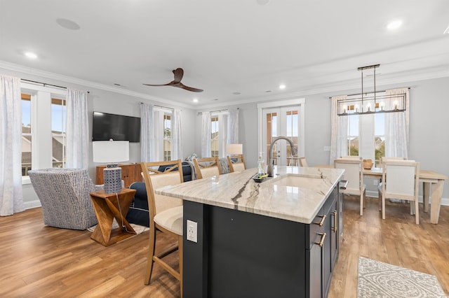 kitchen featuring sink, light hardwood / wood-style flooring, light stone countertops, a center island with sink, and decorative light fixtures