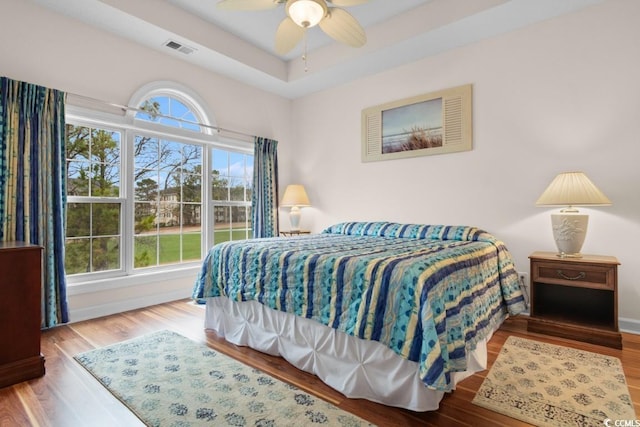 bedroom featuring hardwood / wood-style floors, a raised ceiling, and ceiling fan