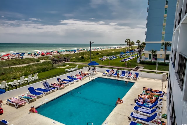 view of pool featuring a patio, a water view, and a beach view