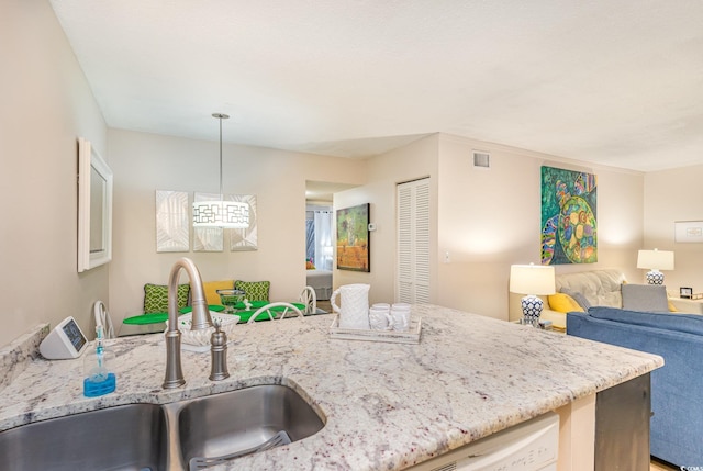 kitchen featuring white dishwasher, sink, decorative light fixtures, and light stone counters