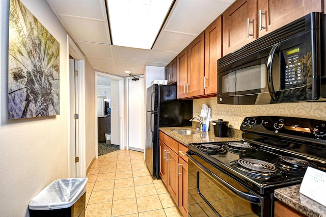 kitchen featuring brown cabinetry, dark stone counters, black appliances, backsplash, and light tile patterned flooring