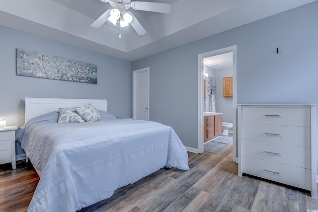 bedroom featuring a tray ceiling, hardwood / wood-style flooring, ceiling fan, and ensuite bathroom