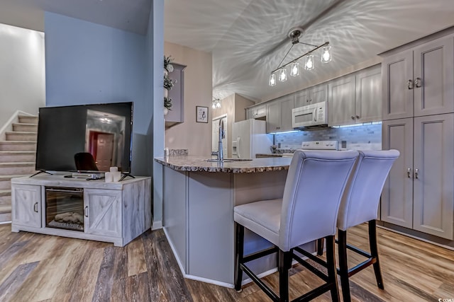 kitchen featuring pendant lighting, white appliances, gray cabinetry, light stone countertops, and kitchen peninsula