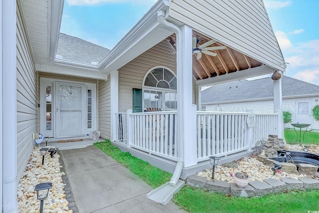 entrance to property with a ceiling fan, a shingled roof, and a porch