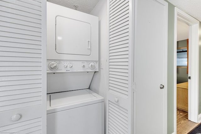 laundry room featuring stacked washer and clothes dryer, hardwood / wood-style floors, and a textured ceiling