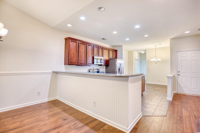 kitchen featuring pendant lighting, light wood finished floors, recessed lighting, appliances with stainless steel finishes, and a peninsula