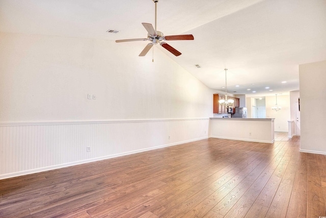 unfurnished living room featuring hardwood / wood-style flooring, lofted ceiling, visible vents, wainscoting, and ceiling fan with notable chandelier