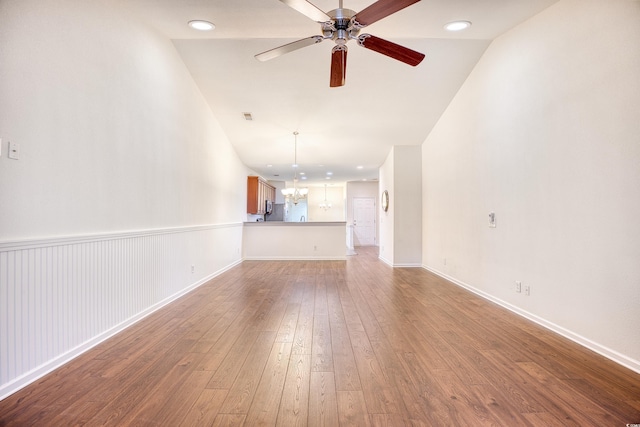 unfurnished living room featuring a wainscoted wall, wood-type flooring, visible vents, baseboards, and ceiling fan with notable chandelier