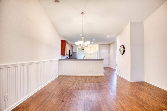 interior space featuring hardwood / wood-style flooring, a peninsula, open floor plan, hanging light fixtures, and an inviting chandelier