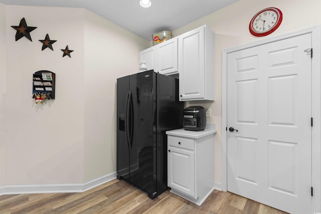 kitchen with white cabinetry, black fridge with ice dispenser, and light wood-type flooring