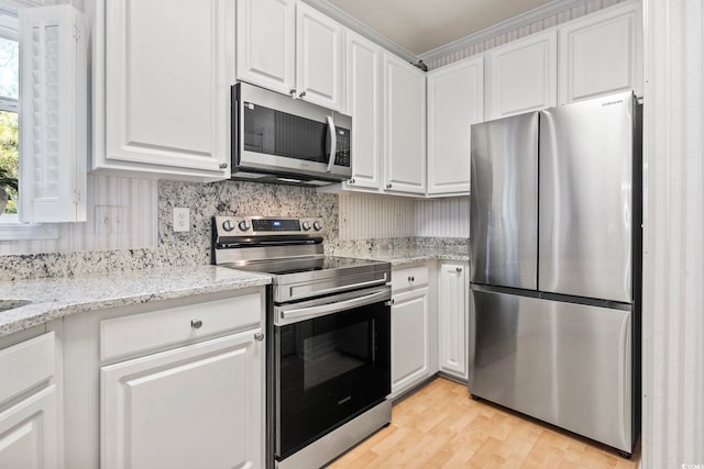 kitchen with appliances with stainless steel finishes, backsplash, white cabinets, light stone counters, and light hardwood / wood-style floors