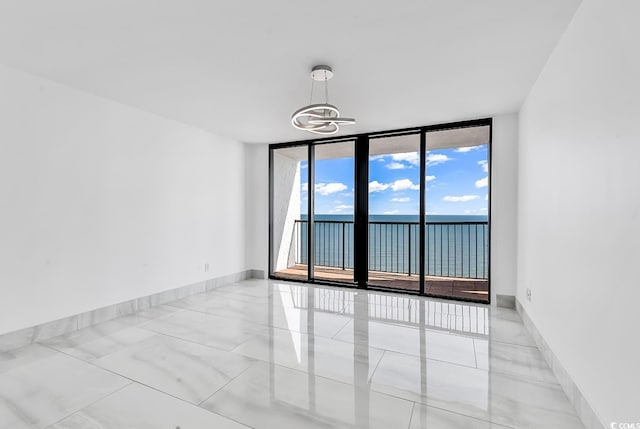 spare room with floor to ceiling windows, a chandelier, and a water view