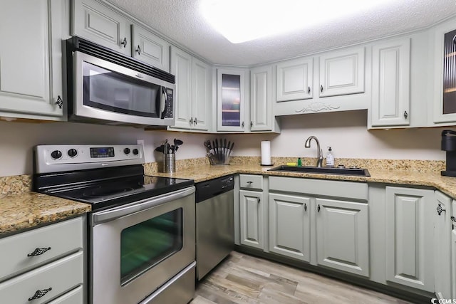 kitchen with stainless steel appliances, a sink, glass insert cabinets, and white cabinets