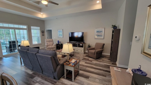 living room featuring ceiling fan, wood-type flooring, a raised ceiling, and a high ceiling