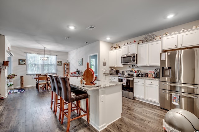 kitchen with hanging light fixtures, appliances with stainless steel finishes, a center island with sink, and white cabinets