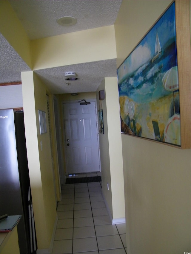 hall with light tile patterned floors, a textured ceiling, and baseboards