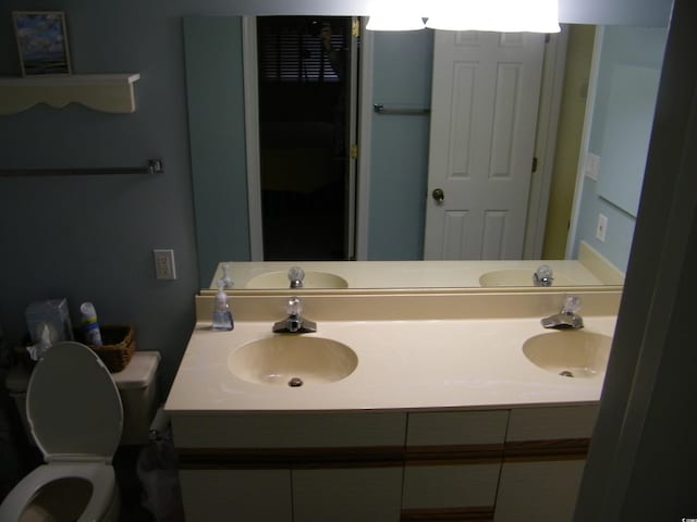 full bath with toilet, double vanity, and a sink