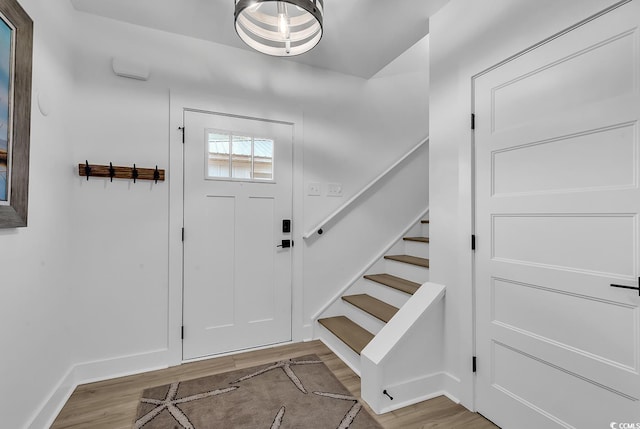 foyer entrance with light wood-type flooring, baseboards, and stairs