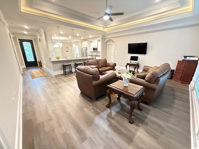 living area with arched walkways, a raised ceiling, ceiling fan, wood finished floors, and baseboards