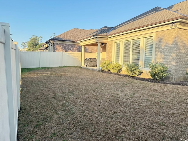 exterior space featuring brick siding, a lawn, a shingled roof, and a fenced backyard