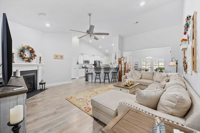 living room featuring ceiling fan with notable chandelier, high vaulted ceiling, and light hardwood / wood-style flooring