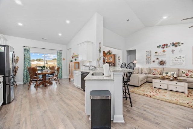 kitchen with sink, a breakfast bar area, stainless steel refrigerator, black dishwasher, and white cabinets