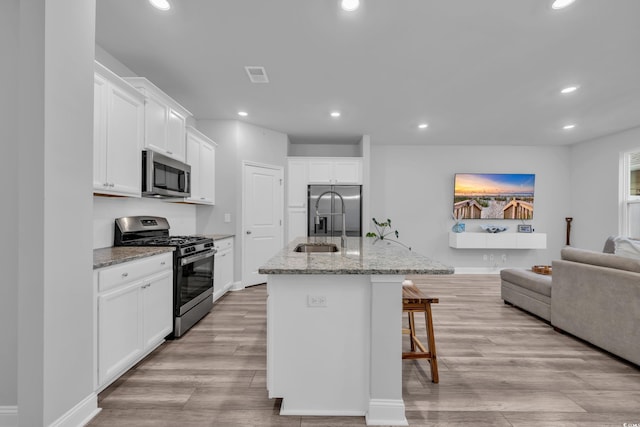 kitchen with a breakfast bar area, white cabinets, a kitchen island with sink, light stone counters, and stainless steel appliances