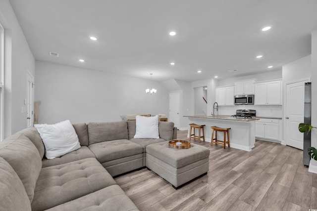 living room featuring sink, an inviting chandelier, and light wood-type flooring