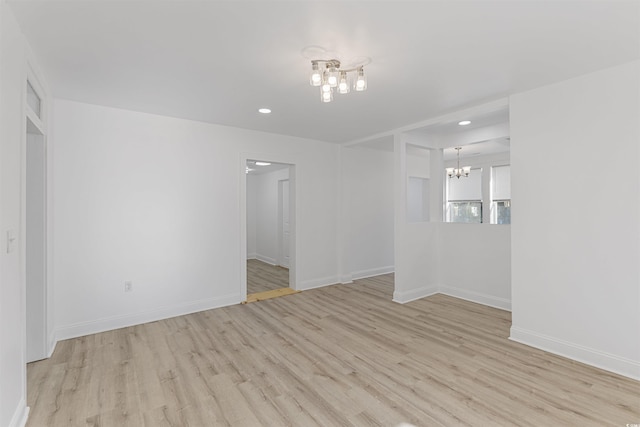 empty room with a notable chandelier, recessed lighting, light wood-type flooring, and baseboards