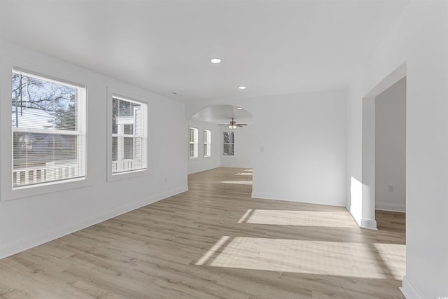 unfurnished living room with light wood finished floors, baseboards, arched walkways, and recessed lighting