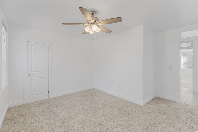 empty room featuring baseboards, a ceiling fan, and light colored carpet