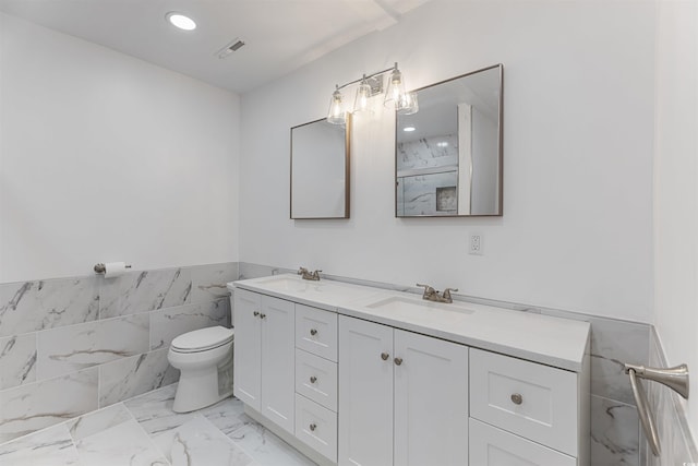 bathroom with marble finish floor, a sink, toilet, and double vanity