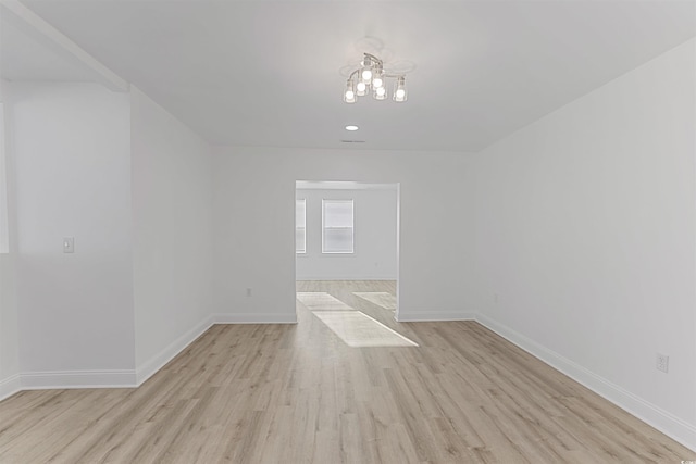 unfurnished room with a notable chandelier, light wood-style flooring, and baseboards