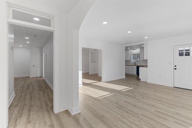 unfurnished living room featuring arched walkways, recessed lighting, a sink, baseboards, and light wood-type flooring