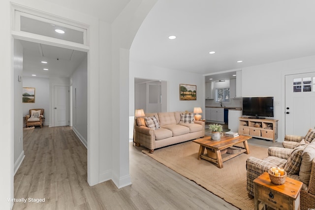 living room featuring light wood-style floors, baseboards, arched walkways, and recessed lighting