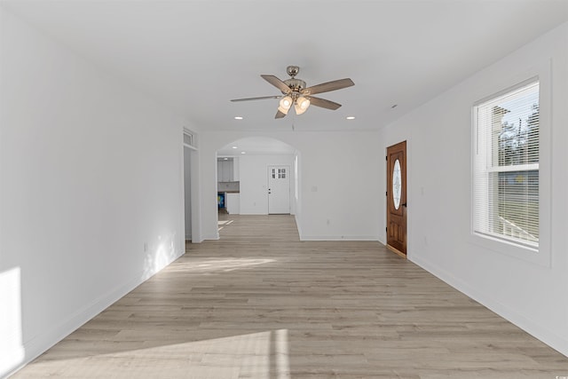 unfurnished living room with light wood finished floors, baseboards, arched walkways, a ceiling fan, and recessed lighting