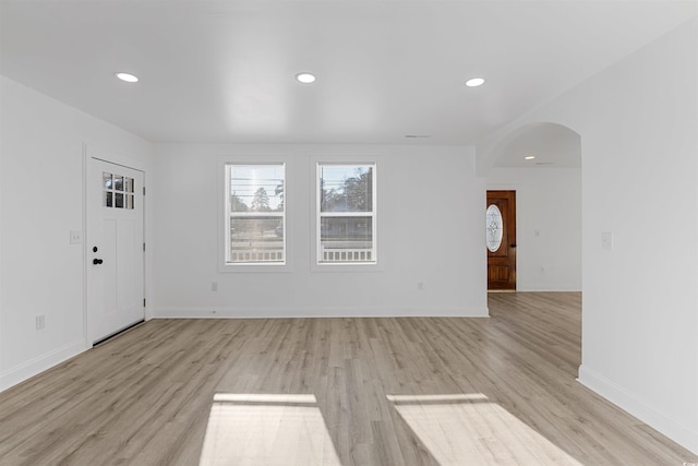 interior space with arched walkways, light wood-style flooring, baseboards, and recessed lighting