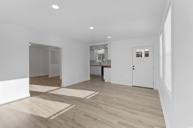 unfurnished living room with baseboards, a sink, light wood-style flooring, and recessed lighting