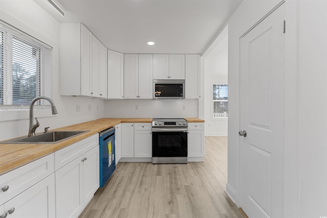 kitchen with stainless steel appliances, butcher block counters, a sink, and white cabinetry