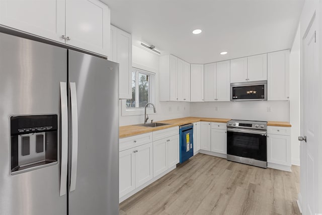 kitchen with wooden counters, appliances with stainless steel finishes, white cabinets, a sink, and light wood-type flooring