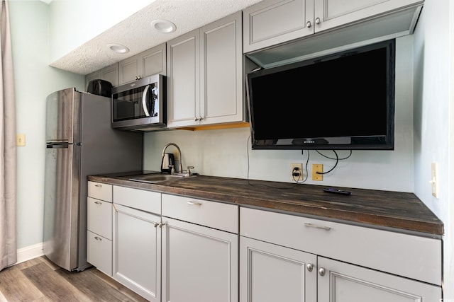 kitchen with a sink, appliances with stainless steel finishes, wood finished floors, and butcher block counters