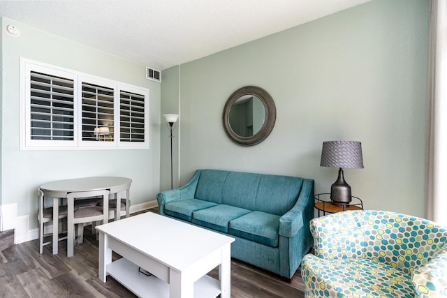 living area with a textured ceiling, dark wood finished floors, visible vents, and baseboards