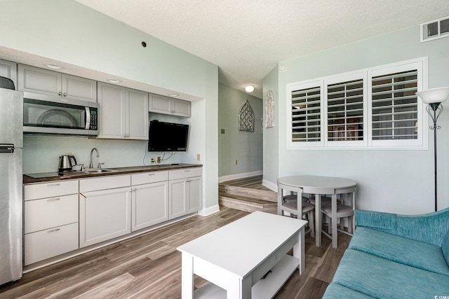 living room with visible vents, a textured ceiling, baseboards, and wood finished floors