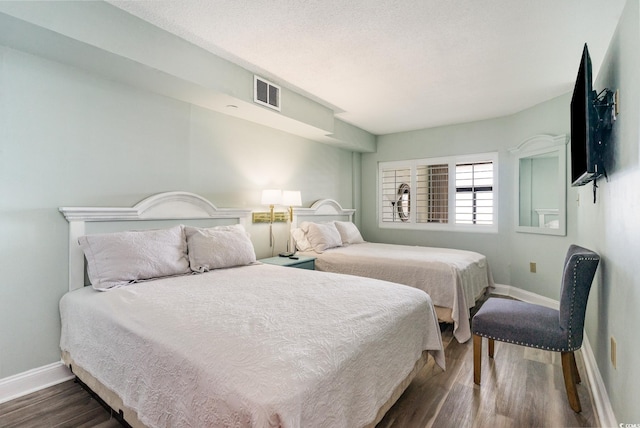 bedroom with dark wood-style flooring, visible vents, a textured ceiling, and baseboards