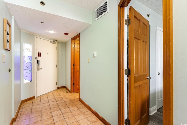 hallway featuring visible vents, a textured ceiling, baseboards, and light tile patterned floors